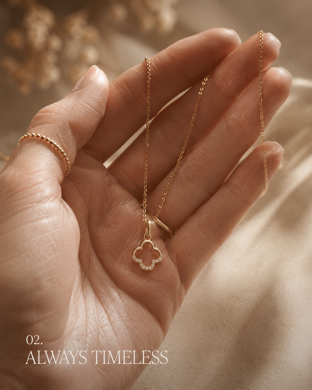 Gold necklace with a clover pendant held in a hand, with 'Always Timeless' text.