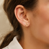 Close-up of an ear wearing a gold floral earring with a blurred background