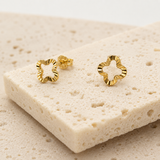 Gold flower-shaped stud earrings with wavy edges on a textured stone surface