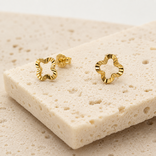 Gold flower-shaped stud earrings with wavy edges on a textured stone surface