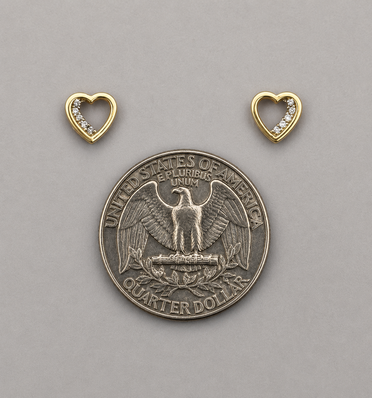 Silver quarter dollar coin with two gold heart-shaped pendants on a gray background
