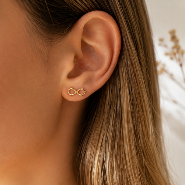 Gold infinity ear cuff on a person's ear with a blurred background