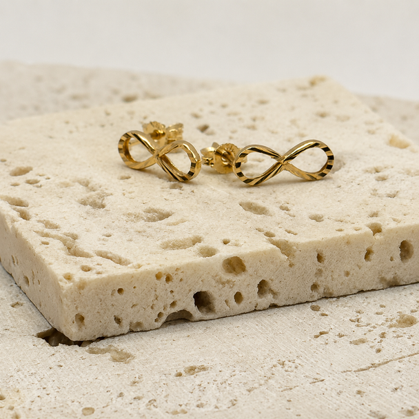 Gold infinity symbol earrings on a textured beige surface