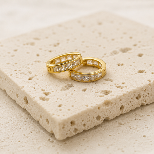 Gold hoop earrings with pave diamonds on a textured stone surface